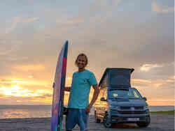 Chris Sammers steht mit Surfbrett vor einem VW California Beach Edition Camper